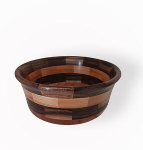 Cuenco de madera artesanal con piezas multitonales flotando sobre fondo blanco con suave sombra